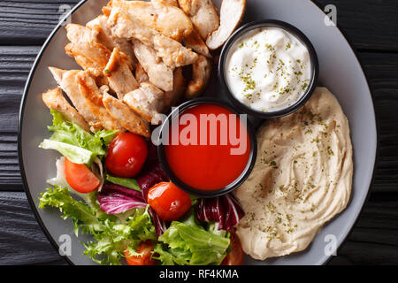 Chicken shawarma mit Hummus, Gemüse und Sauce serviert auf einem Teller close-up auf den Tisch. Horizontal oben Ansicht von oben Stockfoto