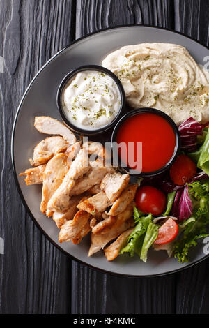 Gesunde shawarma Platte mit Huhn, Hummus, Salat und Saucen close-up auf einem Holztisch. Vertikal oben Ansicht von oben Stockfoto