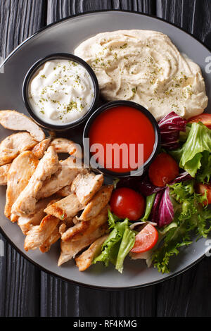 Chicken shawarma mit Hummus, Gemüse und Sauce serviert auf einem Teller close-up auf den Tisch. Vertikal oben Ansicht von oben Stockfoto
