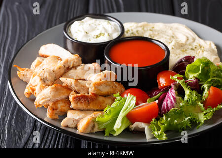 Chicken shawarma mit Hummus, Gemüse und Sauce serviert auf einem Teller close-up auf dem Tisch. Horizontale Stockfoto