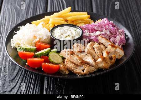 Döner auf einem Teller mit Pommes frites, Salat und Sauce close-up auf einem Holztisch. Horizontale Stockfoto