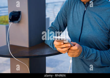 Weibliche mit Telefon und Laden auf einer öffentlichen Ladegerät Stockfoto