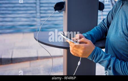 Weibliche mit Telefon und Laden auf einer öffentlichen Ladegerät Stockfoto