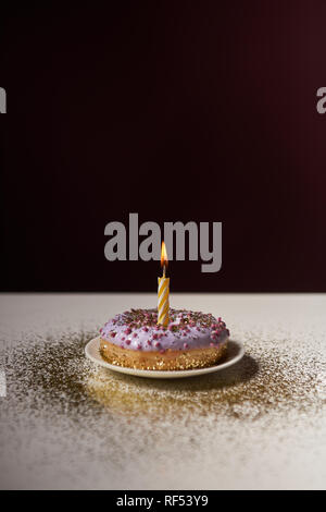 Brennende Kerze in der Mitte der glasierten Krapfen mit goldenen funkelt auf weißen Tisch isoliert auf Schwarz Stockfoto