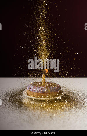 Brennende Kerze in der Mitte der Donut mit fallenden Goldenen funkelt isoliert auf Schwarz Stockfoto