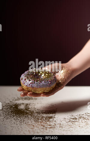 7/8-Ansicht von Frau mit Donut mit goldenen funkelt in Hand isoliert auf Schwarz Stockfoto