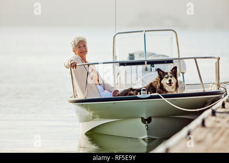 Lächelnd reife Frau entspannt sich auf ein Boot mit ihren großen flauschige Hund. Stockfoto