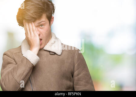 Jungen gutaussehenden Mann tragen Winter Mantel über isolierte Hintergrund Gähnen müde die halbe Gesicht, Augen und Mund mit der Hand. Gesicht weh tut in den Schmerz. Stockfoto