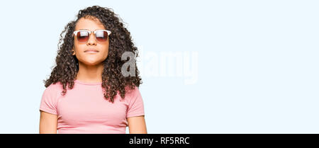 Junge schöne Frau mit lockigem Haar zu tragen rosa Sonnenbrille mit ernsten Gesichtsausdruck. Einfache und natürliche in die Kamera schaut. Stockfoto