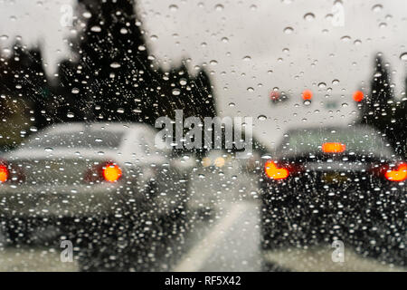 Regentropfen auf der Windschutzscheibe an einem regnerischen Tag; Autos gestoppt an einer Ampel im Hintergrund; Kalifornien Stockfoto