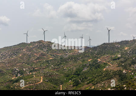 Windenergieanlagen auf Landschaft entlang leere Straße gegen den Himmel. Stockfoto
