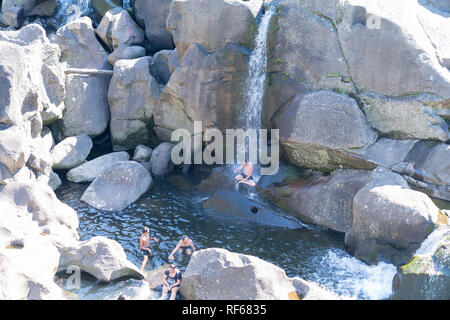 TAURANGA NEUSEELAND - 23. Januar 2019; Genuss an heißen Sommertagen, man sitzt unter malerischen Wasserfall, der auf andere Schwimmer bei McLaren Falls Park Stockfoto