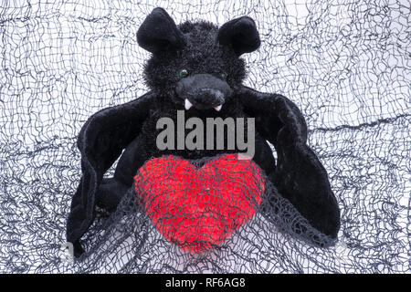 Lustig schwarz bat Spielzeug mit roten flauschigen Herz auf gruselige schwarzes Baumwoll-Stoff gefüllt. Stockfoto