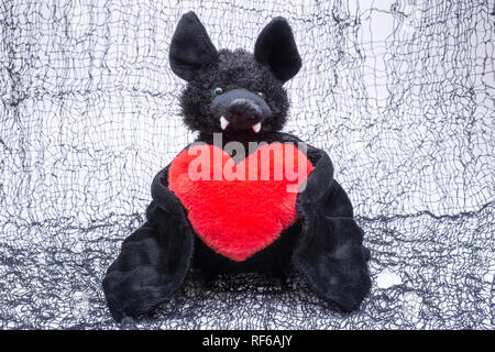 Lustig schwarz bat Spielzeug mit roten flauschigen Herz auf gruselige schwarzes Baumwoll-Stoff gefüllt. Stockfoto