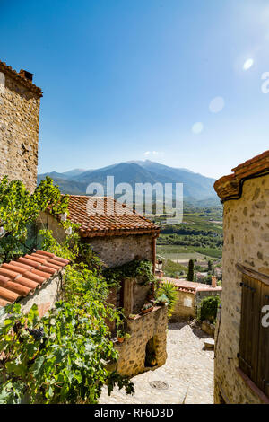 Südfrankreich an einem sonnigen Tag: Eine verträumte Straße im Dorf Eus in der Nähe von der spanischen Grenze mit der französischen Pyrenäen in der Ferne. Stockfoto