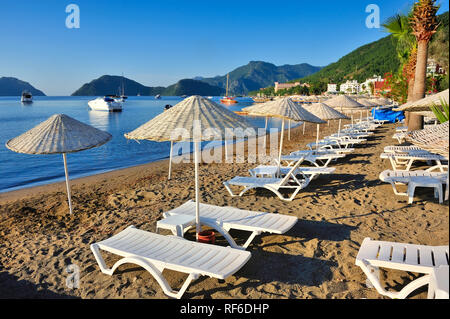 Strand mit Sonnenschirmen und Liegen vor dem Hintergrund der malerischen Bucht von blauem Meer und Berge Stockfoto