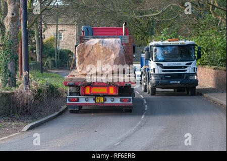 arge-Felsbrocken werden auf einem Flachwagen durch eine Dorfstraße transportiert Stockfoto