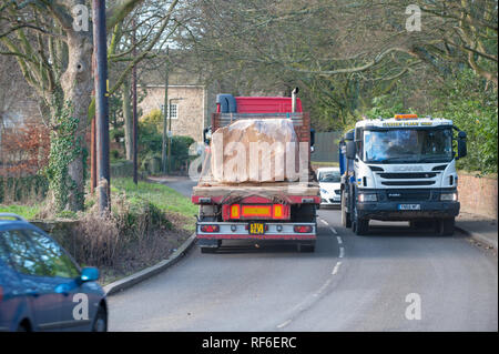 arge-Felsbrocken werden auf einem Flachwagen durch eine Dorfstraße transportiert Stockfoto