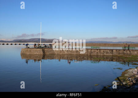 Leute Angeln im Fluss Kent Mündung aus Arnside Pier bei Flut im Januar 2019 mit Arnside Eisenbahnviadukt hinter, Cumbria, Vereinigtes Königreich. Stockfoto