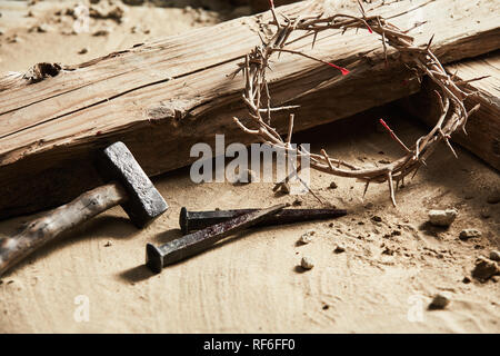 Ostern Hintergrund mit der Darstellung der Kreuzigung mit einem rustikalen hölzernen Kreuz, Hammer, Nägel und Dornenkrone in der Nähe zu 7/8-Ansicht auf Sand Stockfoto