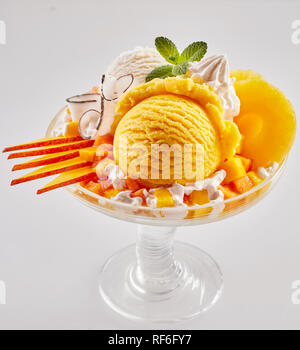 Gourmet handwerklichen frisches Obst Eisbecher mit in Scheiben geschnittenen Mango und Ananas überbacken mit Sahne und Minze im Glas Sockel Teller auf w serviert. Stockfoto