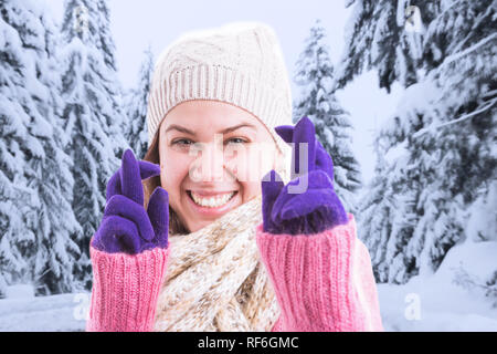 Frau mit hoffnungsvollen Ausdruck winter Kleidung tragen Sie die Haltefinger so viel Glück Geste in lila Handschuhe auf Schnee und Bäume Hintergrund gekreuzt Stockfoto