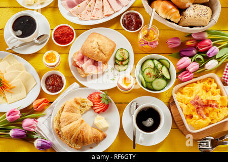 Gesunden Frühling Frühstück für Zwei mit Blick auf einen Tisch mit einem Croissant, Speck, Brötchen, Aufschnitt, Käse, verschiedene Marmeladen ein Stockfoto