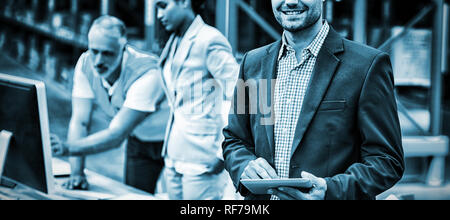 Fokus auf Manager lächelt und hält eine Tablette vor seinen Kollegen Stockfoto