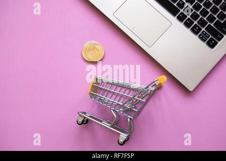 Konzeptionelle Foto von e-commerce mit cryptocurrency. Computer, Einkaufswagen und Bitcoin Münzen oder cryptocurrency auf eine trendige rosa Hintergrund. Stockfoto