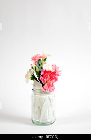 Eine kleine Gruppe von roten, weißen und rosa Nelke Blume Reste in ein Marmeladenglas mit Küchentuch gesäumt. Stockfoto