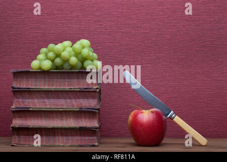 Alte Bücher, Apple mit einem Messer und Trauben auf dem Burgund Hintergrund. Stockfoto