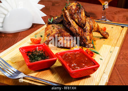 Appetitlich Tabak Huhn auf einem Holzbrett mit Cherry Tomaten und zwei Arten von Saucen. Close-up Stockfoto