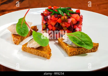 Vinaigrette Salat auf einem weißen Teller mit Roggen Brot Toast mit Schichten von Hering und Mangold verlässt. Seite Ansicht von oben. Close-up Stockfoto