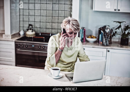 Ältere Frau Gespräch am Handy mit Laptop Stockfoto