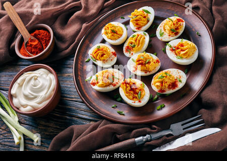 Nahaufnahme der Russische Eier bestreut mit Paprika und gehackten Frühlingszwiebeln auf einem Steingut Teller auf einem alten rustikalen Holztisch mit braunem Stoff, Stockfoto