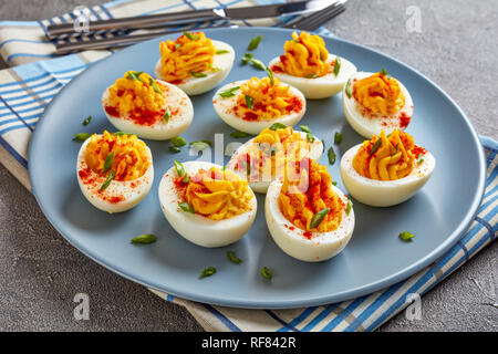 Russische Eier bestreut mit Paprika und Frühlingszwiebeln, fein gehackt auf einem grauen Platte auf einer konkreten Tabelle, horizontale Ansicht von oben, close-up Stockfoto