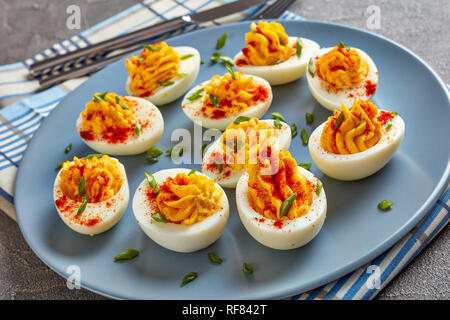 Russische Eier bestreut mit Paprika und Frühlingszwiebeln, fein gehackt auf einem grauen Platte auf einer konkreten Tabelle, horizontale Ansicht von oben, close-up Stockfoto