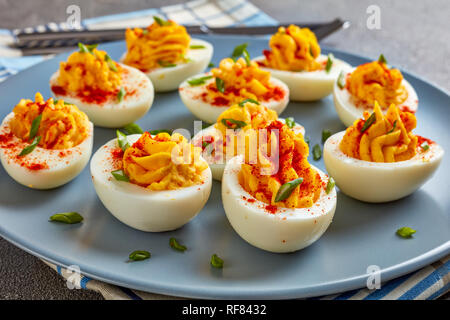 Russische Eier bestreut mit Paprika und Frühlingszwiebeln, fein gehackt auf einem grauen Platte auf einer konkreten Tabelle, horizontale Ansicht von oben, Nah-, Makro Stockfoto