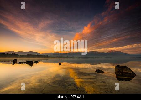 Forggensee mit Reflexion der bewölkten Himmel und die Allgäuer Berge im Hintergrund bei Sonnenaufgang, Füssen, Allgäu, Bayern Stockfoto