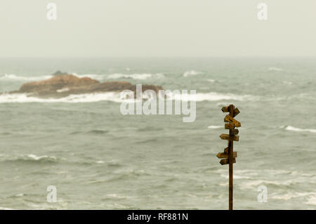 Hölzerne Wegweiser mit vielen Zeiger mit dem Meer im Hintergrund. Stockfoto