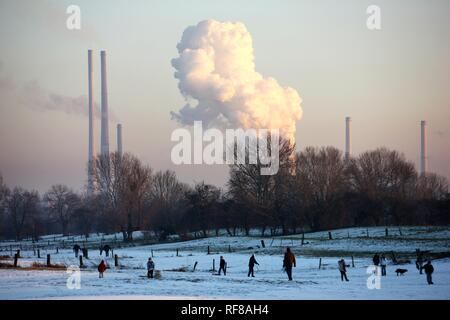 Childred spielen auf eine gefrorene Wiese im Winter, Thyssen-Krupp Stahlwerk im Hintergrund, Duisburg, Nordrhein-Westfalen Stockfoto