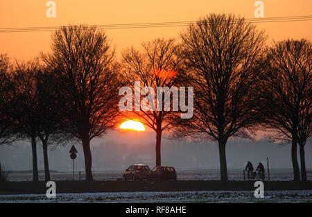 Sonnenuntergang, Autofahrer und Radfahrer auf einer Landstraße im Winter in der Nähe von Duisburg, Nordrhein-Westfalen Stockfoto