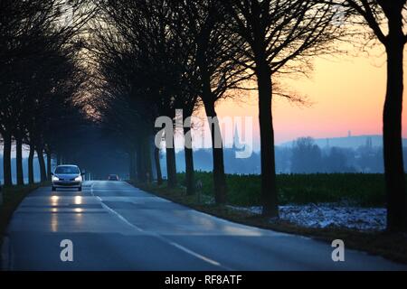 Auto Fahren auf einer Landstraße bei Sonnenuntergang im Winter in der Nähe von Duisburg, Nordrhein-Westfalen Stockfoto