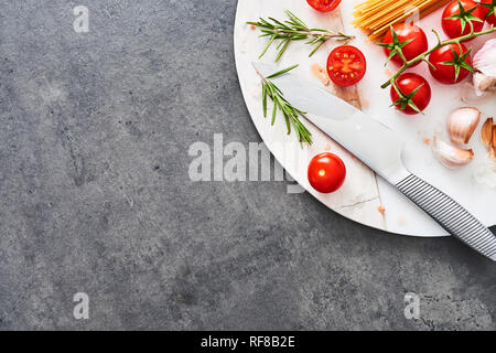 Italienisches Essen Hintergrund. Ungekocht integral Spaghetti, Tomaten, Rosmarin, Knoblauch und Himalaya Salz auf weißem Marmor Platte über dunkle konkrete Tabelle. Ingr Stockfoto
