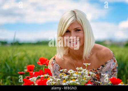 Eine schöne, attraktive, blonde Frau sammelt Wiese Blumen am Rand des Feldes. Soft Focus. Stockfoto