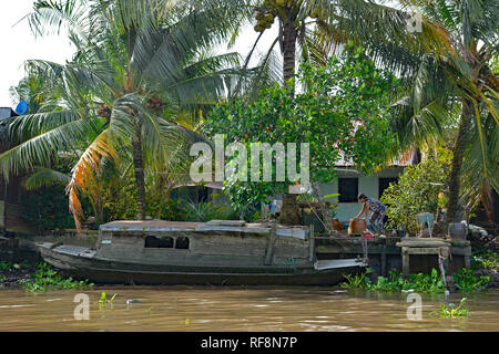 Can Tho, Vietnam - am 31. Dezember 2017. Ein Boot günstig außerhalb eines Hauses im Mekong Delta. Eine Frau bewegt sich einige große Töpfe am Ufer im Hintergrund Stockfoto