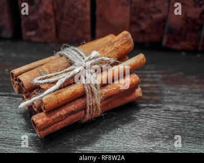 Drei Zimtstangen mit Jute Seil auf einem schwarzen Holztisch gebunden. Stockfoto