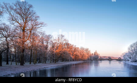 Leipzig im Frost, vereister Fluss Weiße Elster und Palmengartenwehr im roten Licht der aufgehenden Sonne Stockfoto