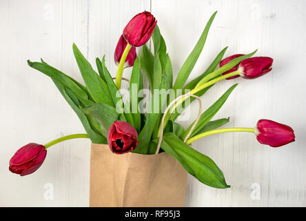 Nahaufnahme der rote Tulpe Blumenstrauß im generischen braune Papiertüte auf gekalkten Holz Hintergrund Stockfoto