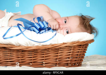 Adorable Baby Boy im Weidenkorb mit blauer Schleife Stockfoto
